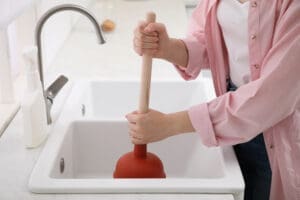woman using plunger in her sick to clear a clogged drain