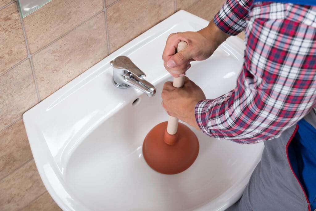 Close-up Of A Plumber Using Plunger In Bathroom Sink